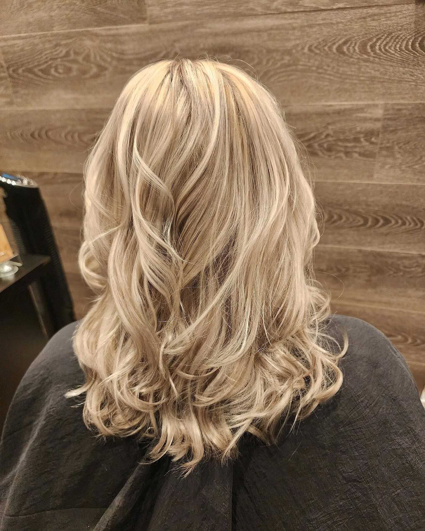Blonde hair with loose waves viewed from the back against a wooden wall background.
