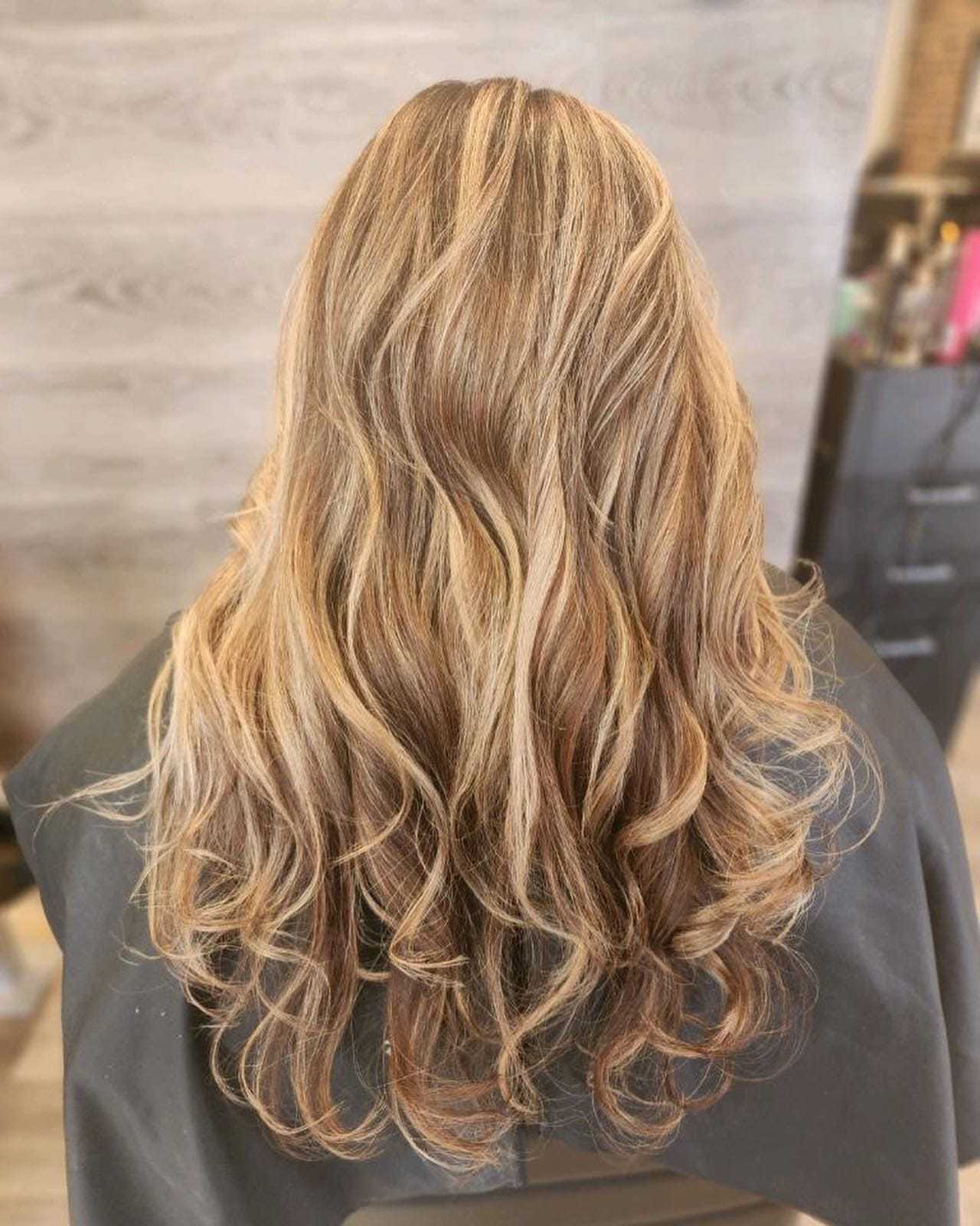 Long, wavy highlighted hair cascading down a salon cape.